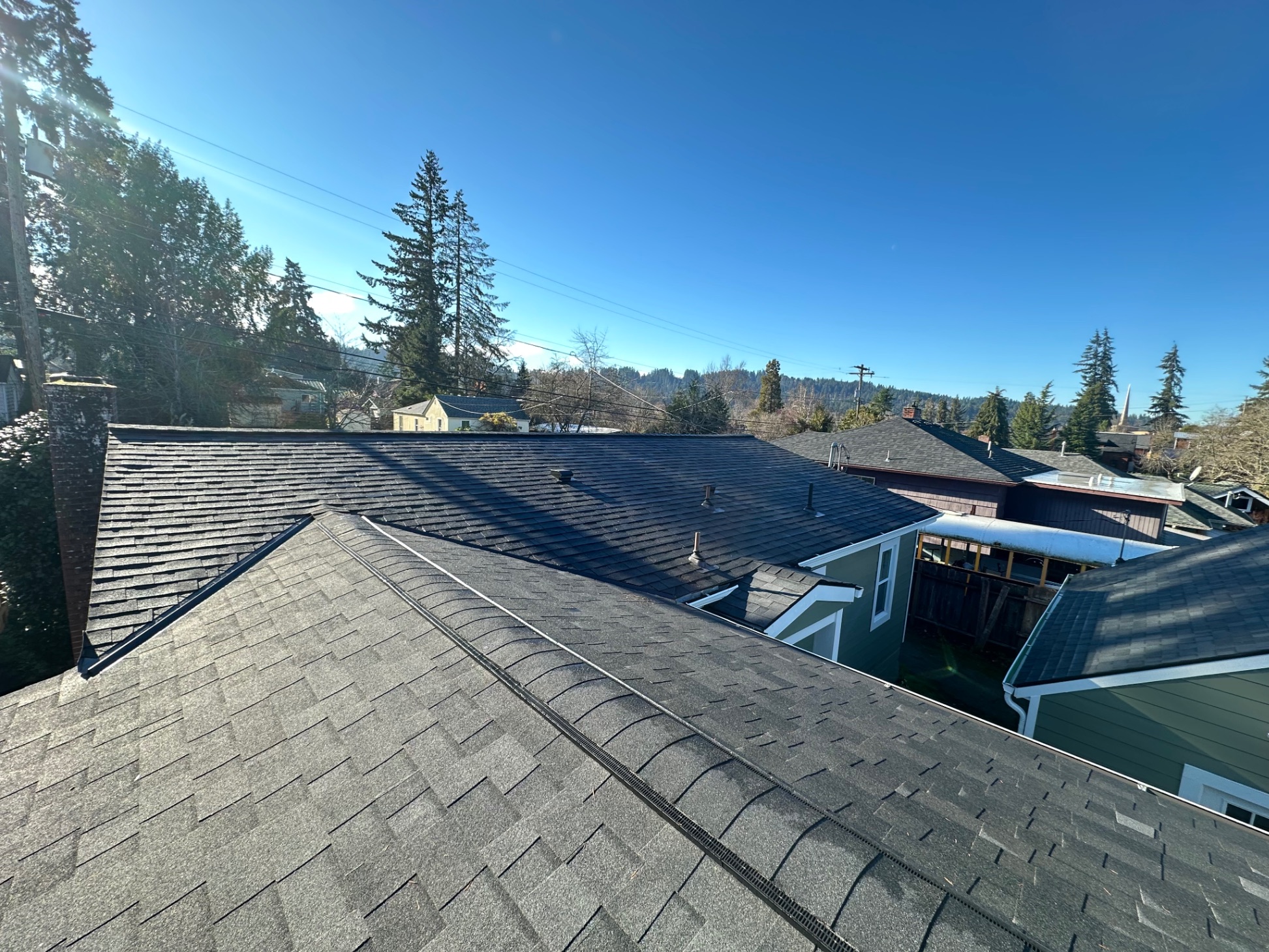 Completed charcoal shingle roof installation with mountain backdrop — Newport, OR by Firu Construction LLC